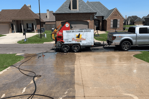 Bayou Bins truck and trailer performing trash bin cleaning in a residential driveway