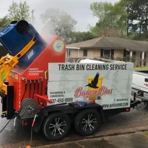 Professional trash bin cleaning truck spraying hot water to clean a blue garbage can in a residential neighborhood.