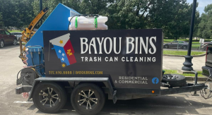 A black trailer for Bayou Bins Trash Can Cleaning, with a blue bin lifter, white water tank, and logo.