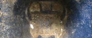 A close-up, dark and grimy shot looking down into a blue drain with water and detritus at the bottom.