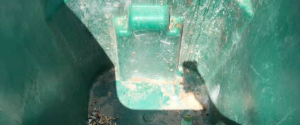 Looking down into a dirty, empty green recycling bin with some debris on the bottom.