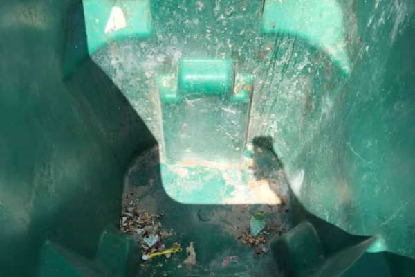 A close-up, top-down view inside a dirty, empty green plastic trash can with some debris at the bottom.